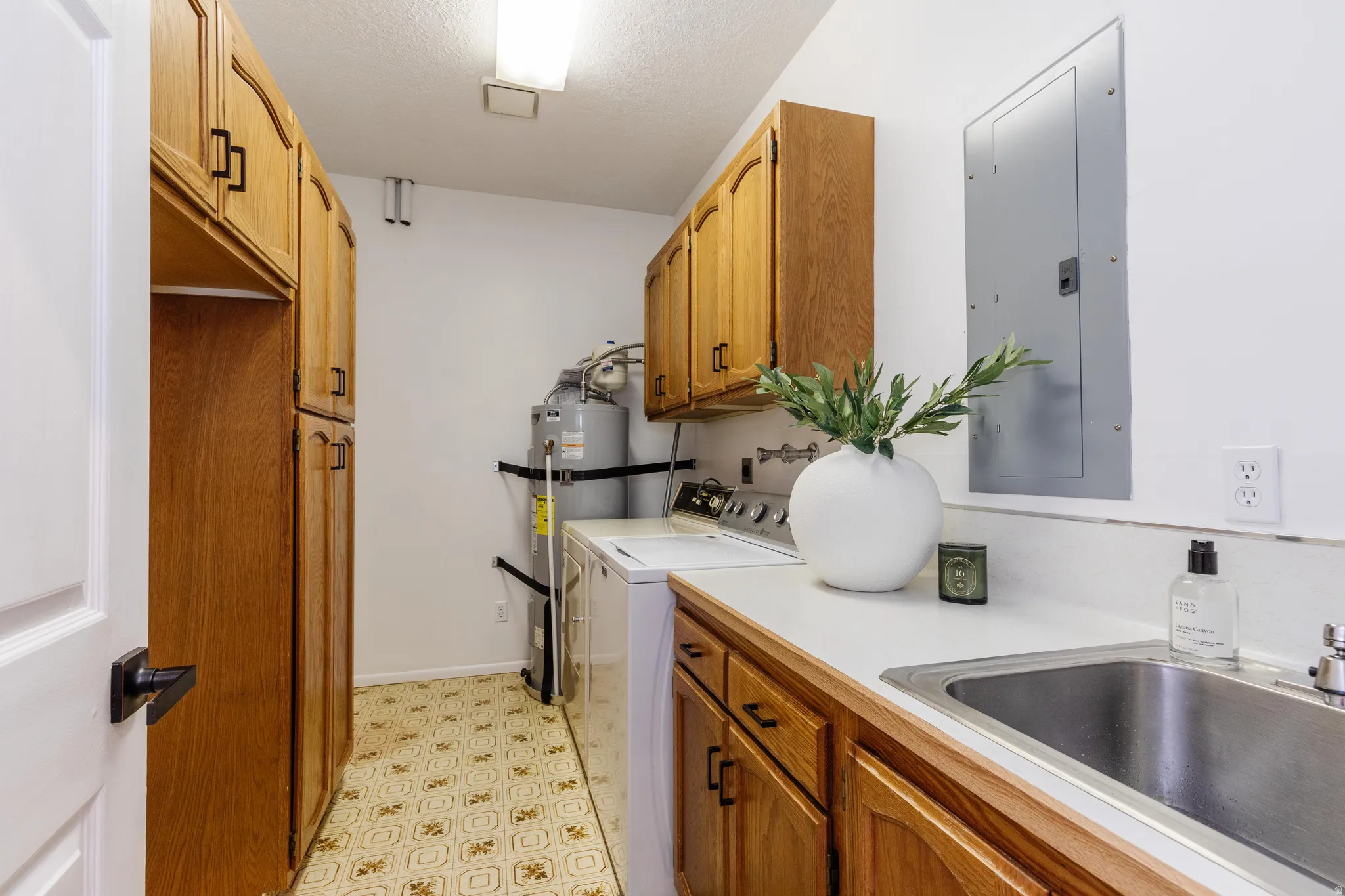Utility room featuring extensive wood cabinetry, a utility sink with a stainless steel basin, and white countertops