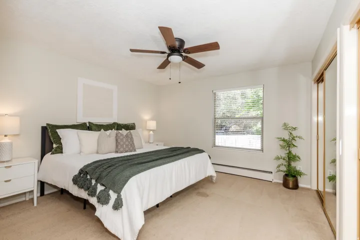 Carpeted bedroom featuring a window with blinds, a ceiling fan with integrated lighting, and a mirrored closet door