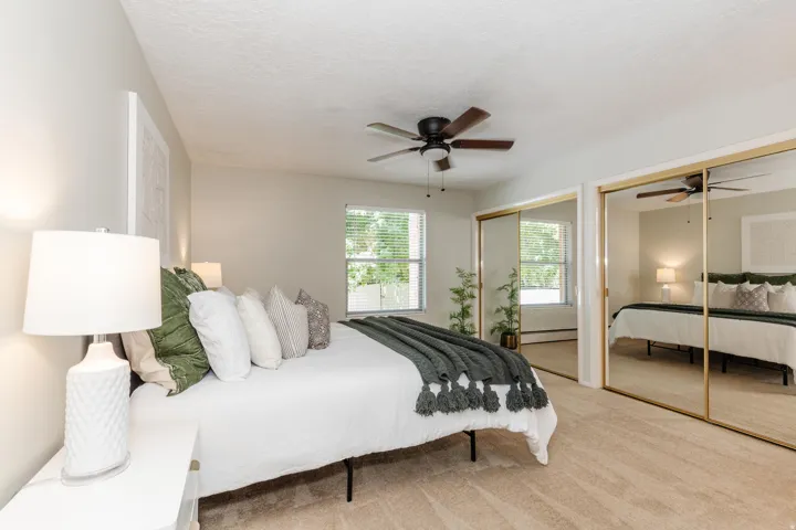 Carpeted bedroom with a ceiling fan, window with blinds, and mirrored sliding closet doors