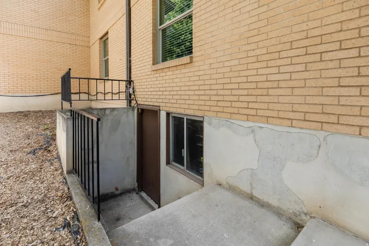 Concrete stairs leading to a brown entry door, flanked by a rectangular window, set against a light brick exterior