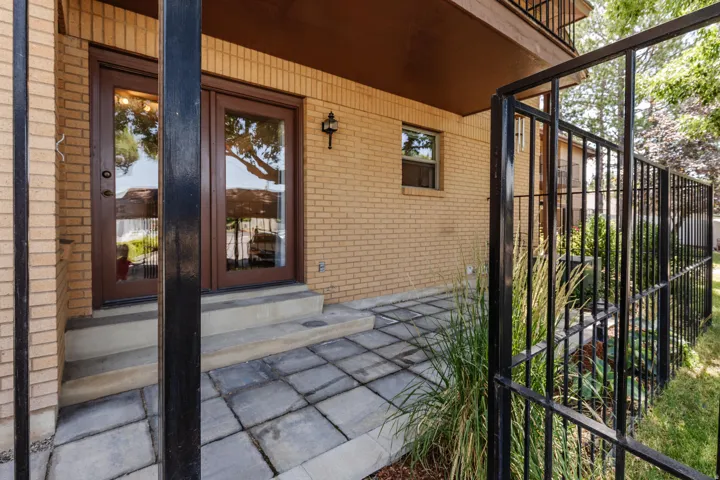 Brick exterior featuring a private patio with paver stones, brown-framed double doors, a black wrought-iron fence, and established landscaping