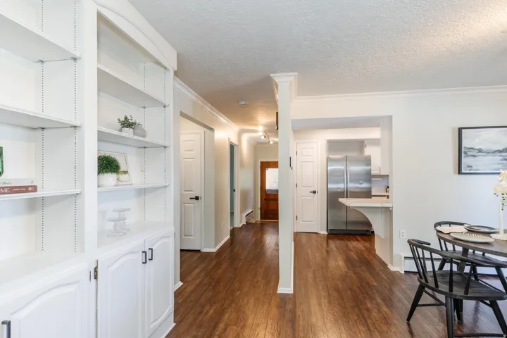 Built-in white shelving with lower cabinetry, wood-finish flooring, white crown molding, recessed lighting, and a kitchen featuring stainless steel appliances