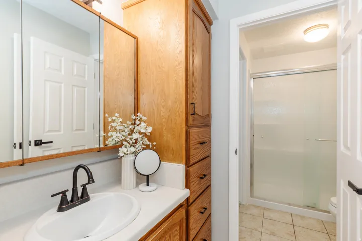 Bathroom featuring a light wood vanity with a white countertop and oval sink, matte black faucet, and mirrored medicine cabinet