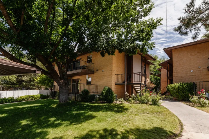 Exterior brick building with individual balconies, a covered outdoor area, and a large mature tree