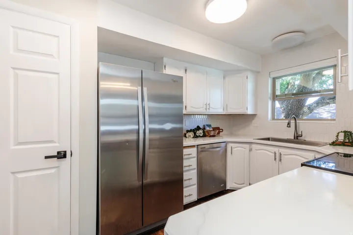 Kitchen featuring stainless steel appliances, white cabinetry, a white tile backsplash, and light countertops