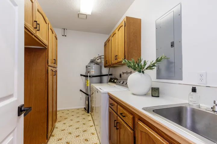 Utility room featuring extensive wood cabinetry, a utility sink with a stainless steel basin, and white countertops