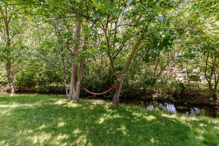 Lush green lawn bordered by mature trees and a natural water feature