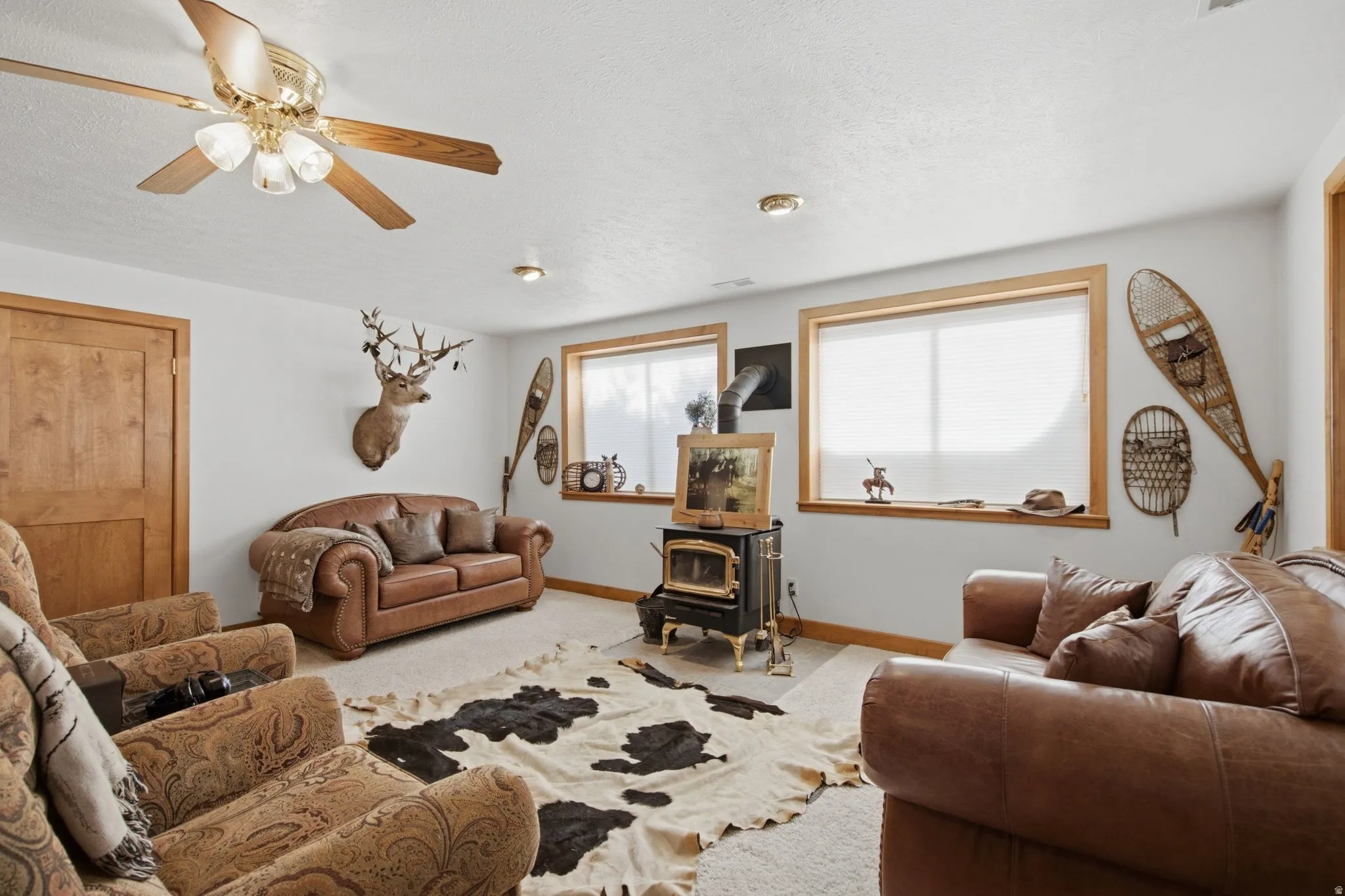 Living area featuring a freestanding wood-burning stove, two windows with wood trim, a wood-paneled door, recessed lighting, and a ceiling fan with integrated lighting