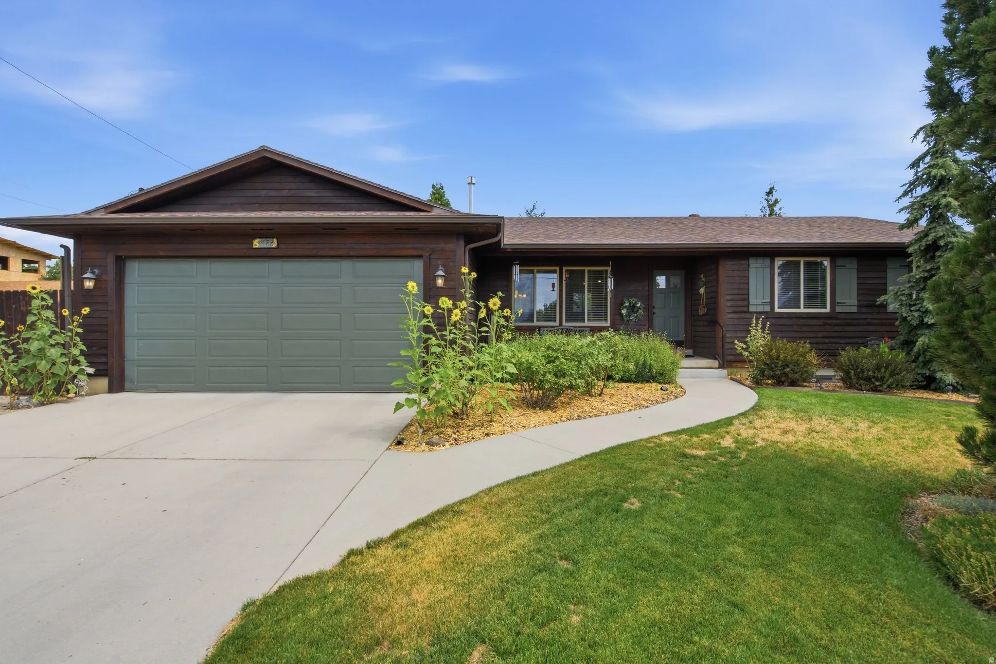 Ranch-style residence featuring brown wood-paneled siding, a dark asphalt shingle roof, and a light gray concrete driveway