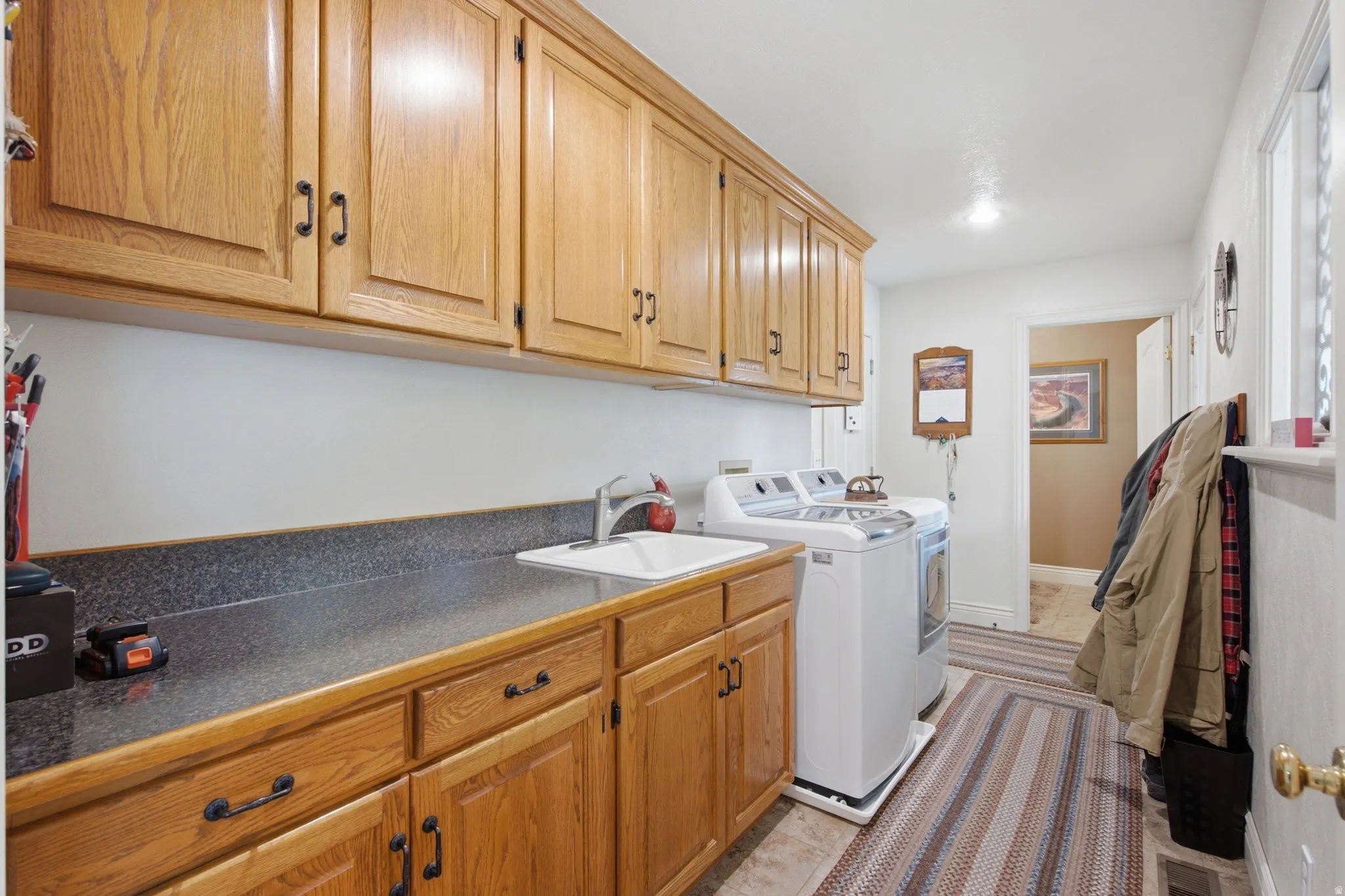 Laundry area featuring ample wood-finish cabinetry, dark speckled countertops, and an integrated utility sink with a chrome faucet