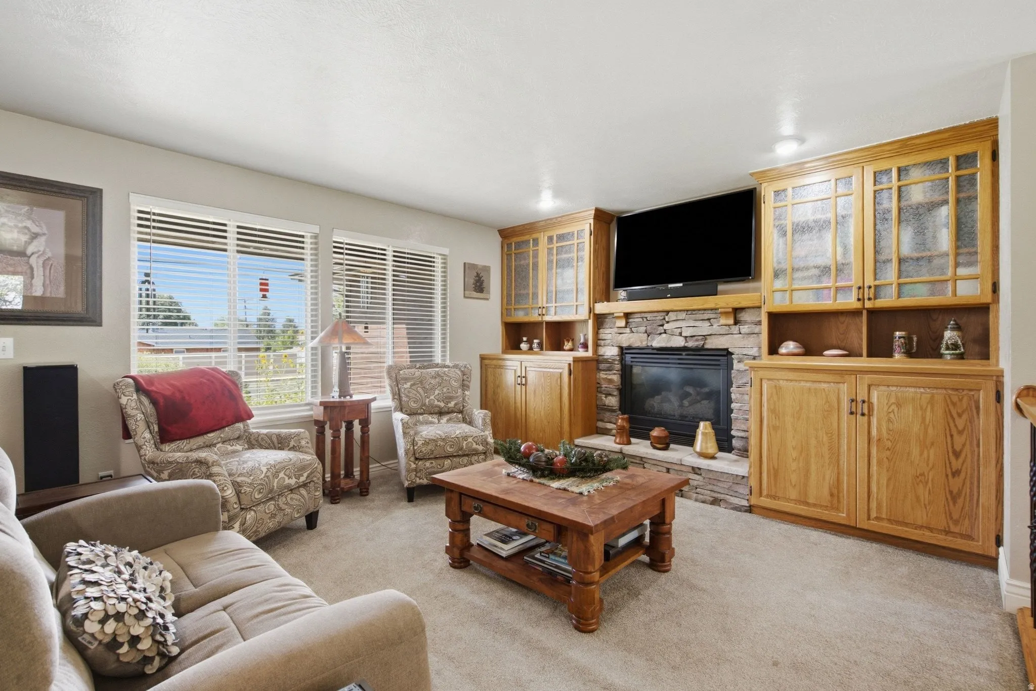 Living room featuring a stone-surround fireplace with a wood mantel, flanked by extensive built-in cabinetry with both solid and glass-front doors