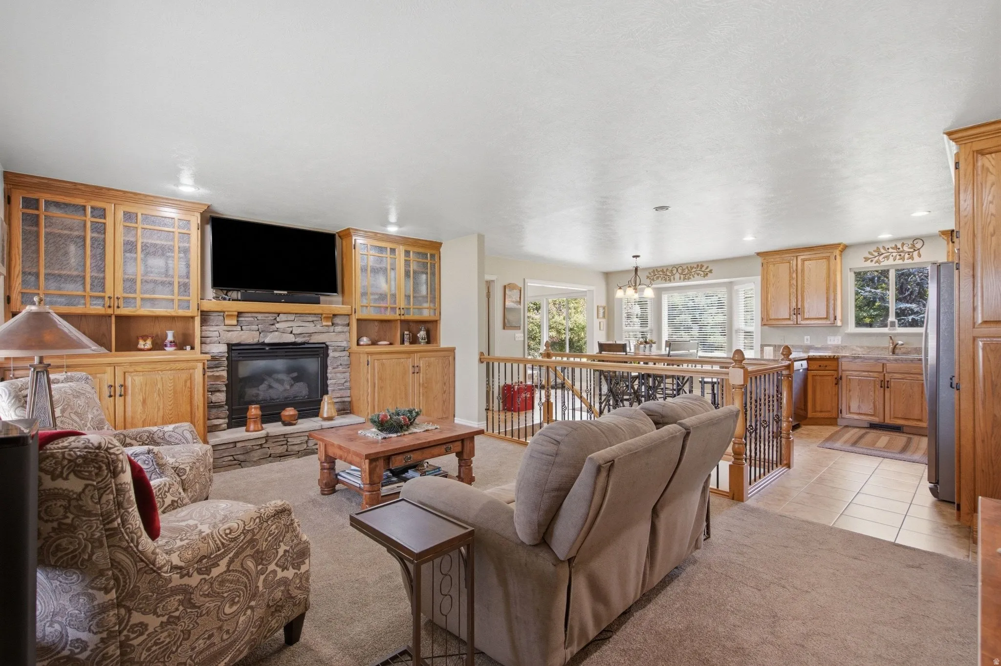 Warm living area featuring a stone-faced fireplace with wood mantel, flanked by built-in wood cabinetry with glass-front uppers