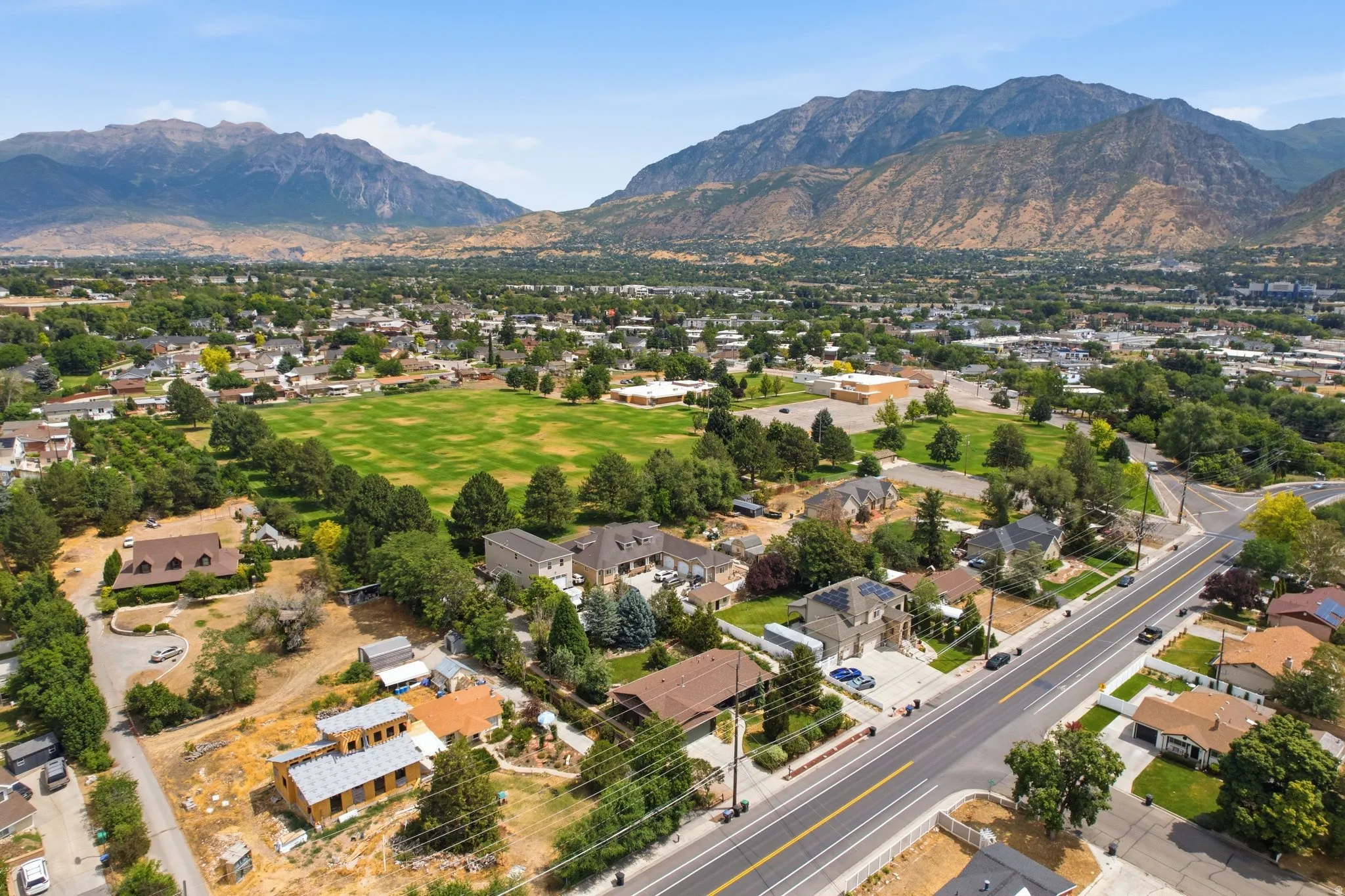 Expansive neighborhood setting featuring a large open green space, mature trees, and a prominent mountainous backdrop