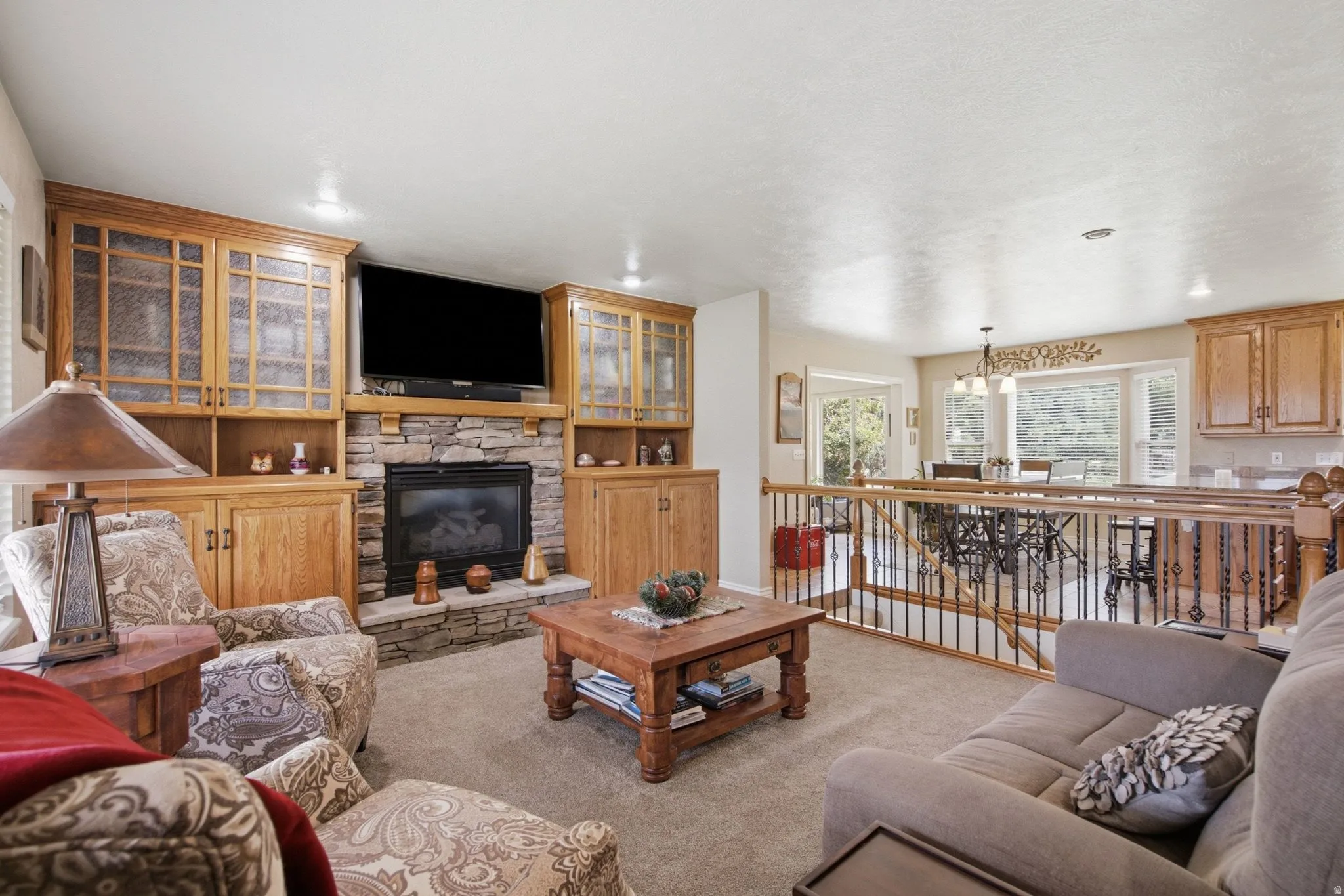 Living area featuring a stone-clad fireplace and hearth with built-in wood cabinetry and glass-front upper cabinets