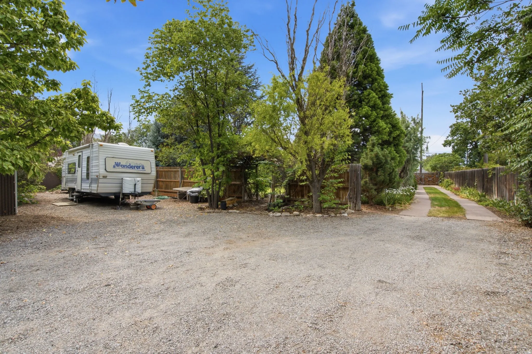 Expansive gravel parking area with mature trees and a fenced perimeter
