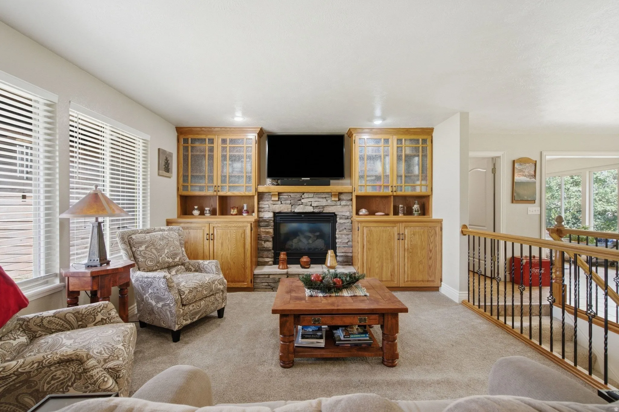 Living area featuring a stone-clad fireplace and hearth, flanked by built-in wood cabinetry with glass-front uppers