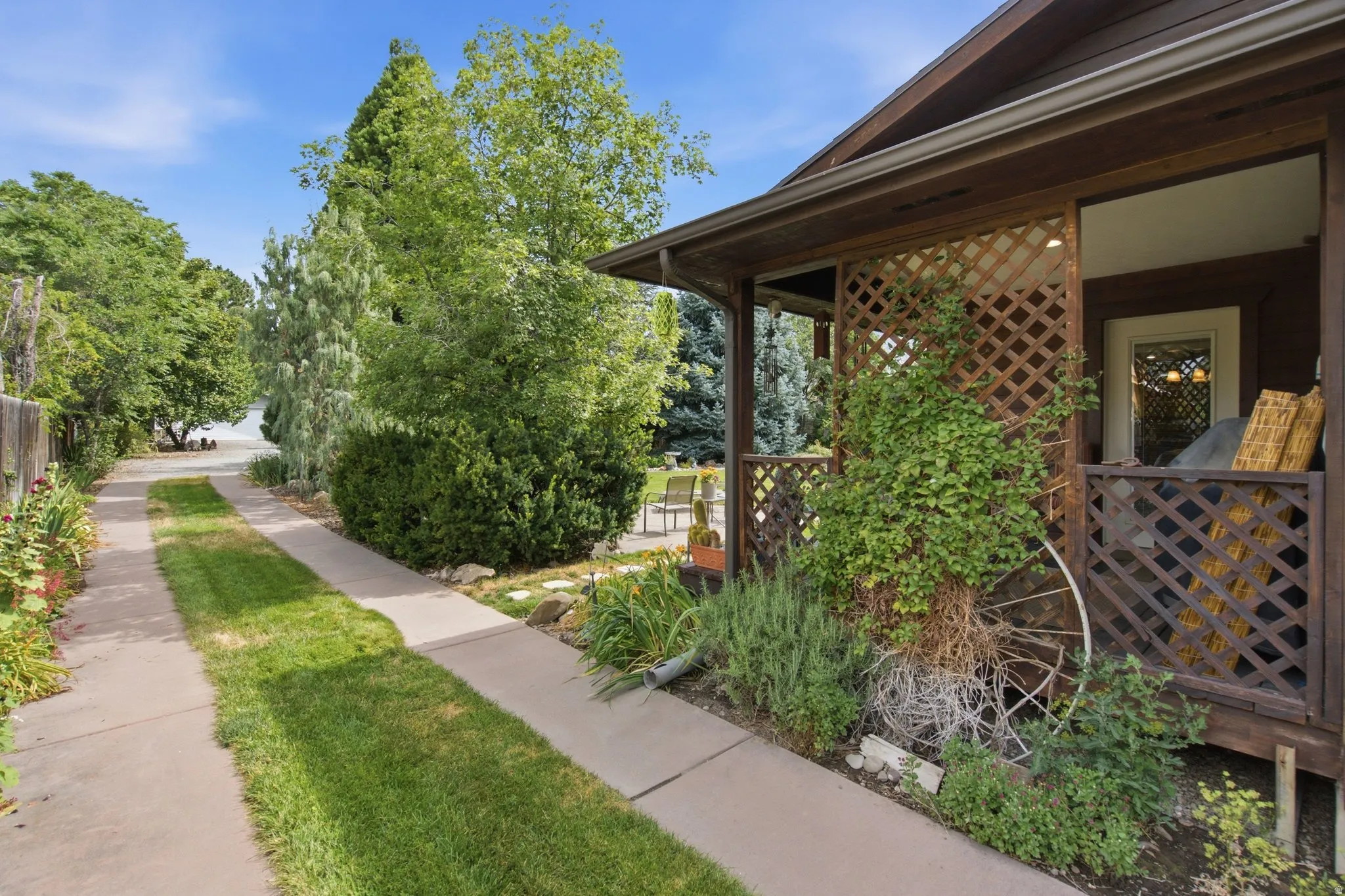 Exterior featuring a covered porch with lattice screening, mature landscaping, and a concrete driveway with a central grass strip