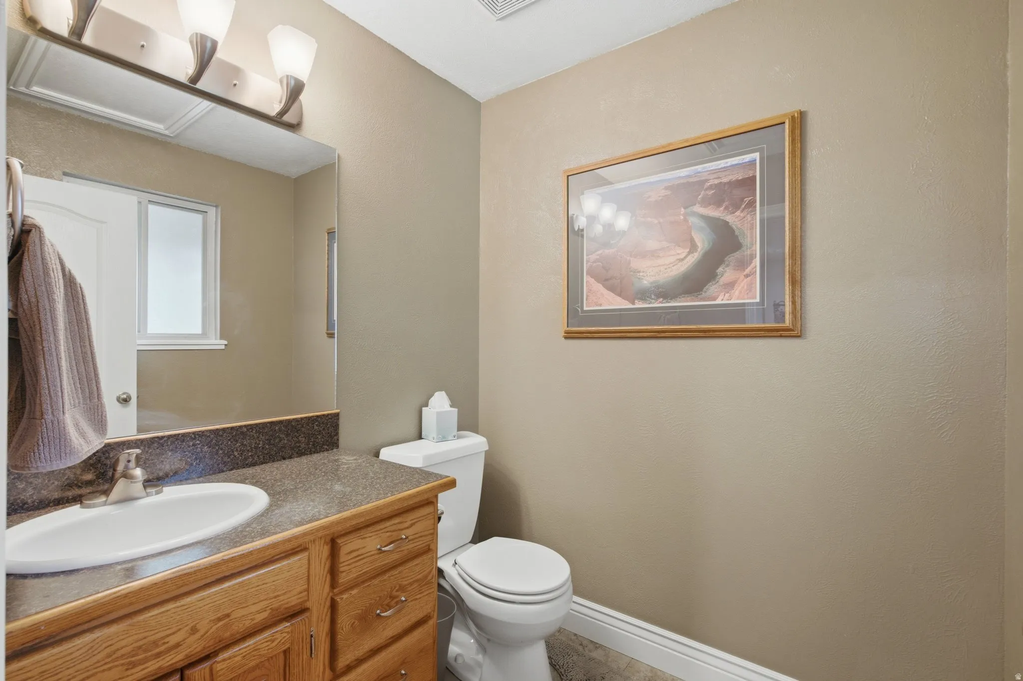 Bathroom featuring a single vanity with wood cabinetry and a dark speckled countertop, an undermount sink, and a framed wall mirror