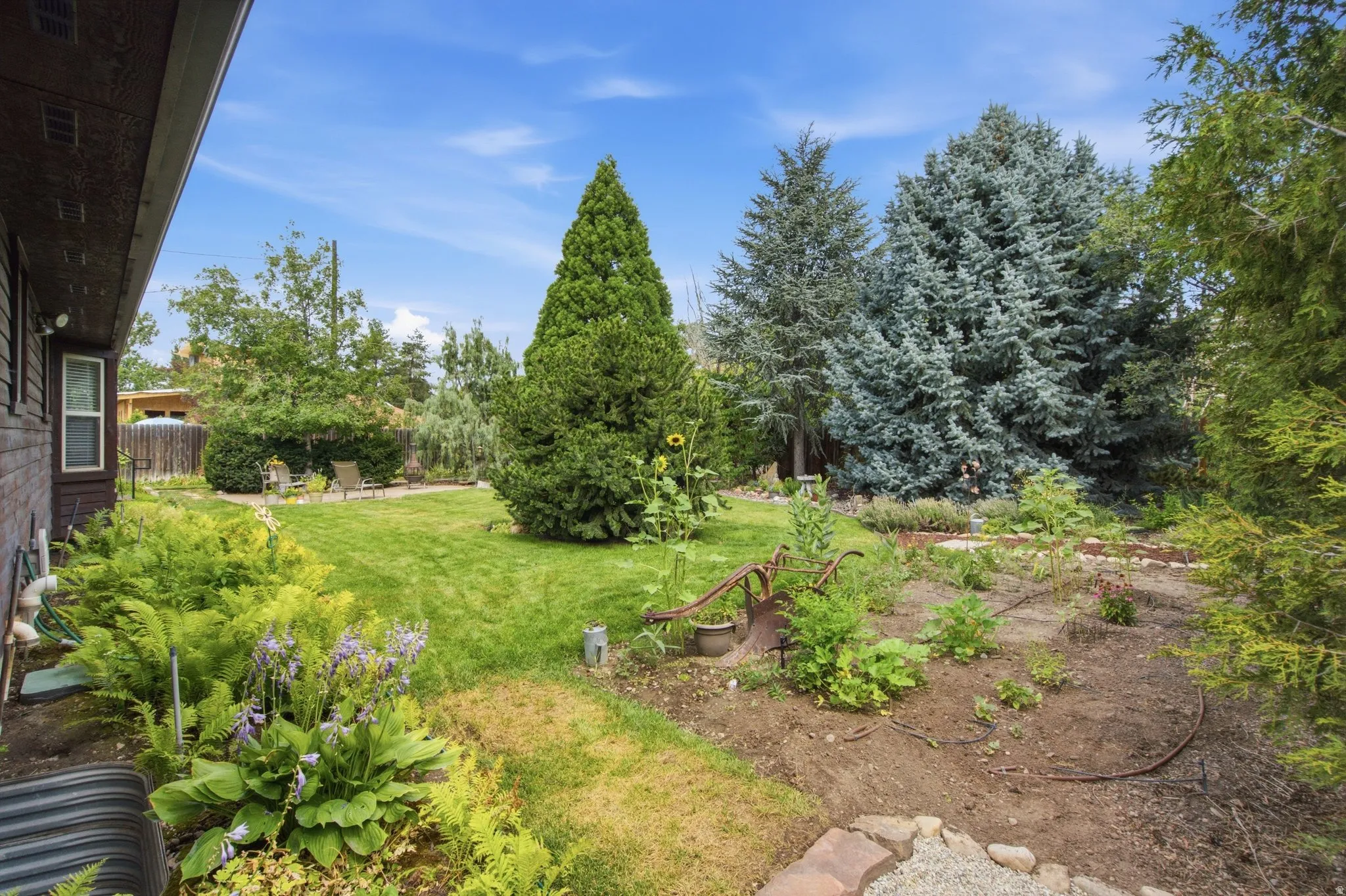 Expansive backyard featuring a manicured lawn, established garden beds, and mature trees
