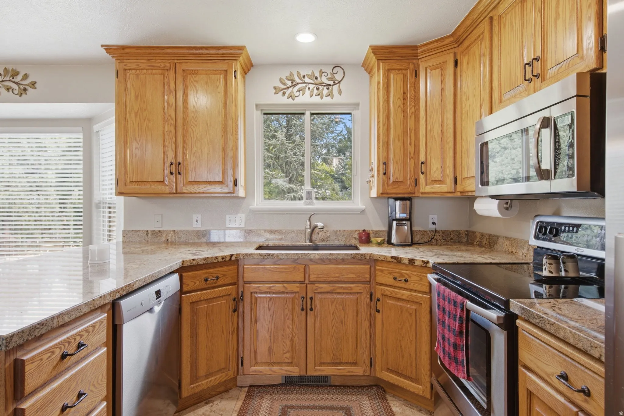 Kitchen featuring light wood cabinetry, granite-style countertops, stainless steel appliances, and a window above the sink