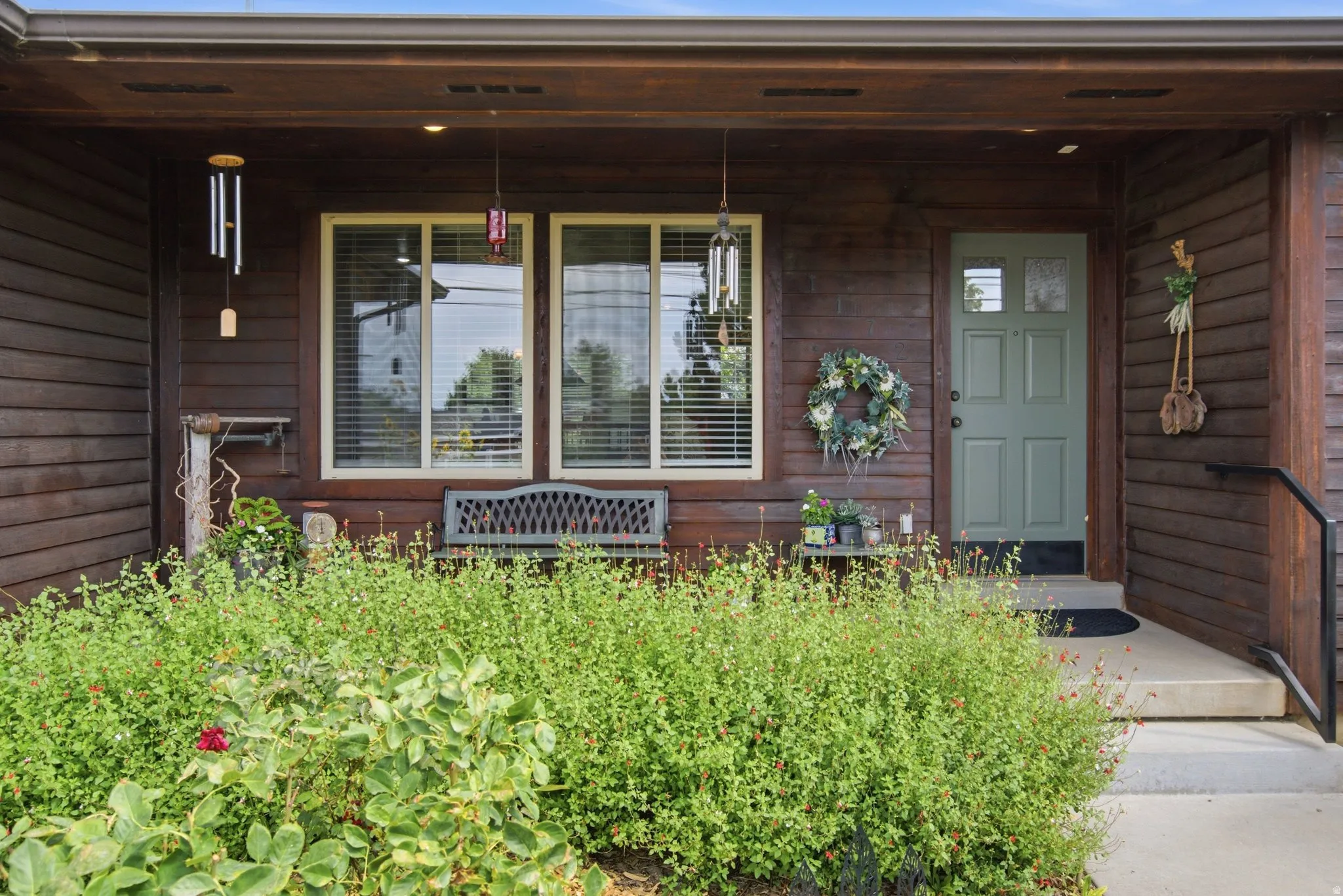 Covered front entry featuring a wood-panel exterior, a pale green front door with clear glass panels, and a concrete porch with a black metal handrail
