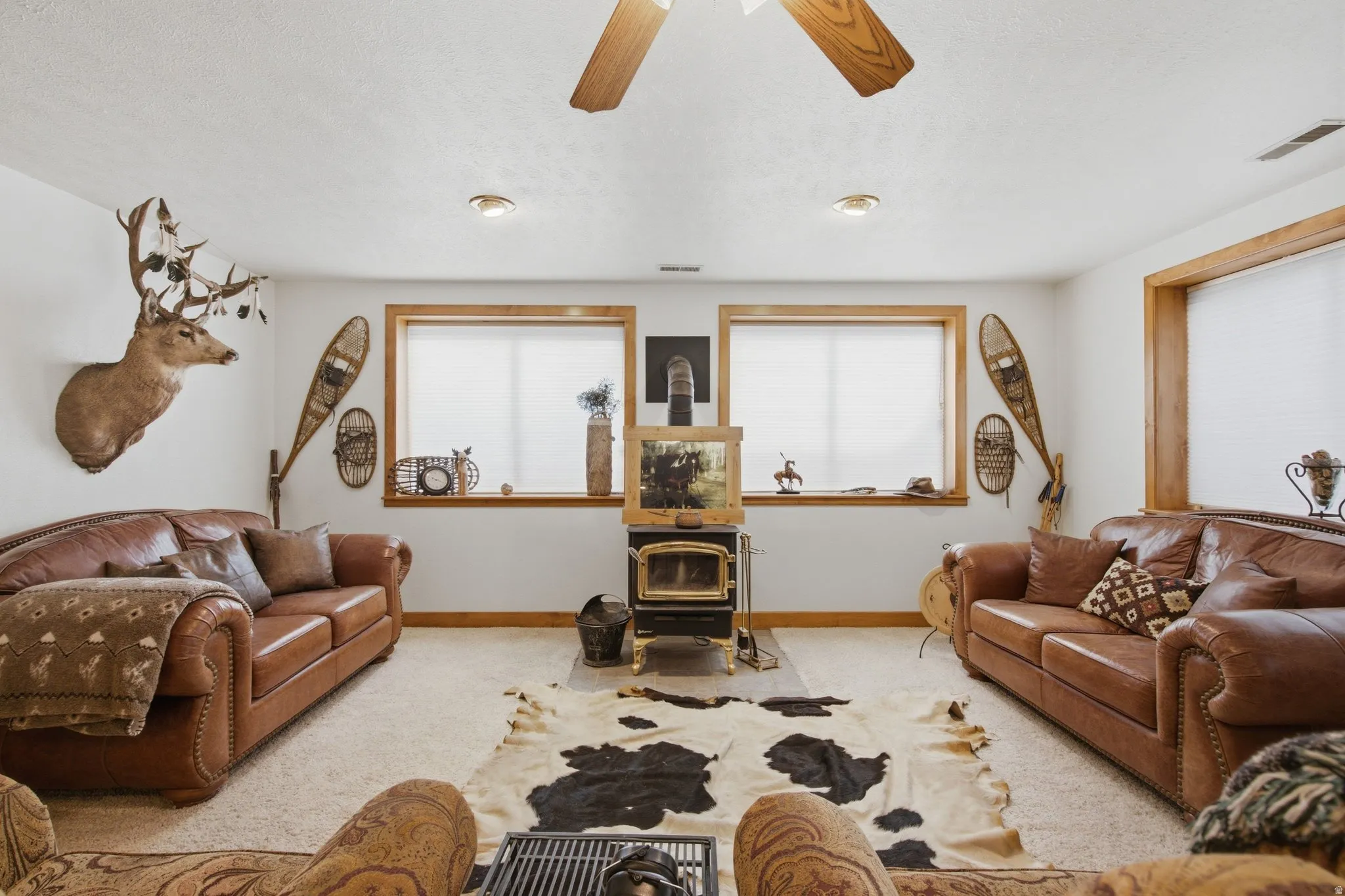 Spacious room featuring a wood-burning stove, two windows with wood trim, recessed lighting, and a ceiling fan