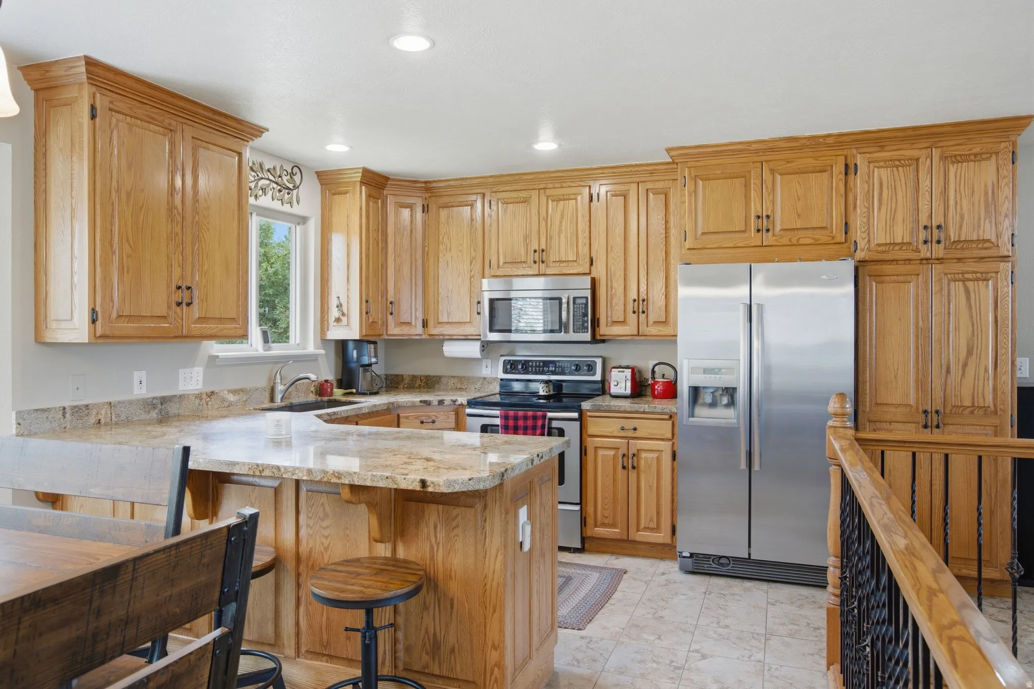 Kitchen featuring wood cabinetry, stainless steel appliances, a double basin sink, and a U-shaped peninsula with a breakfast bar