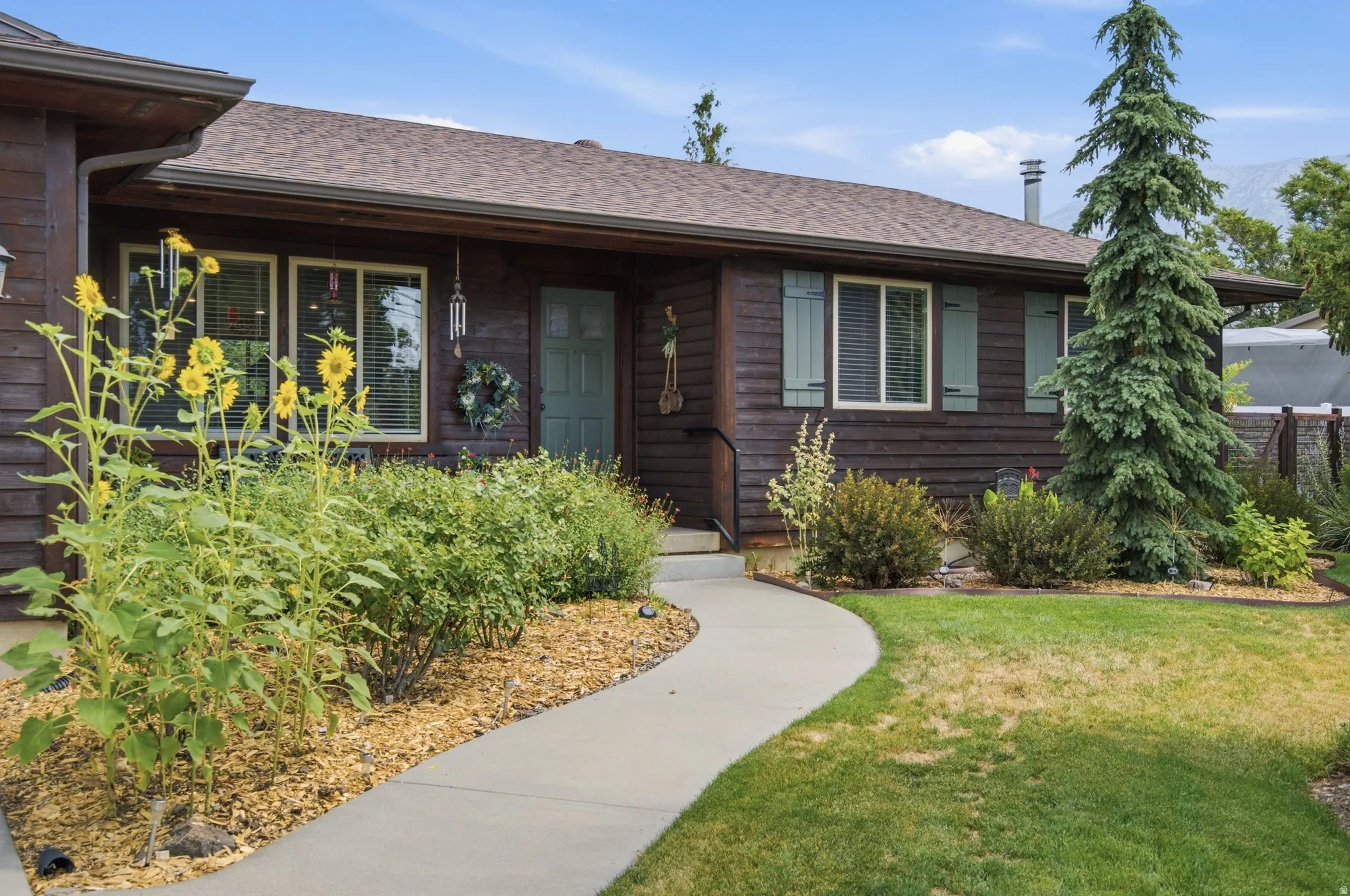 Wood-sided exterior featuring a front entry door with transom window, accent shutters, multiple windows, and a curved concrete walkway
