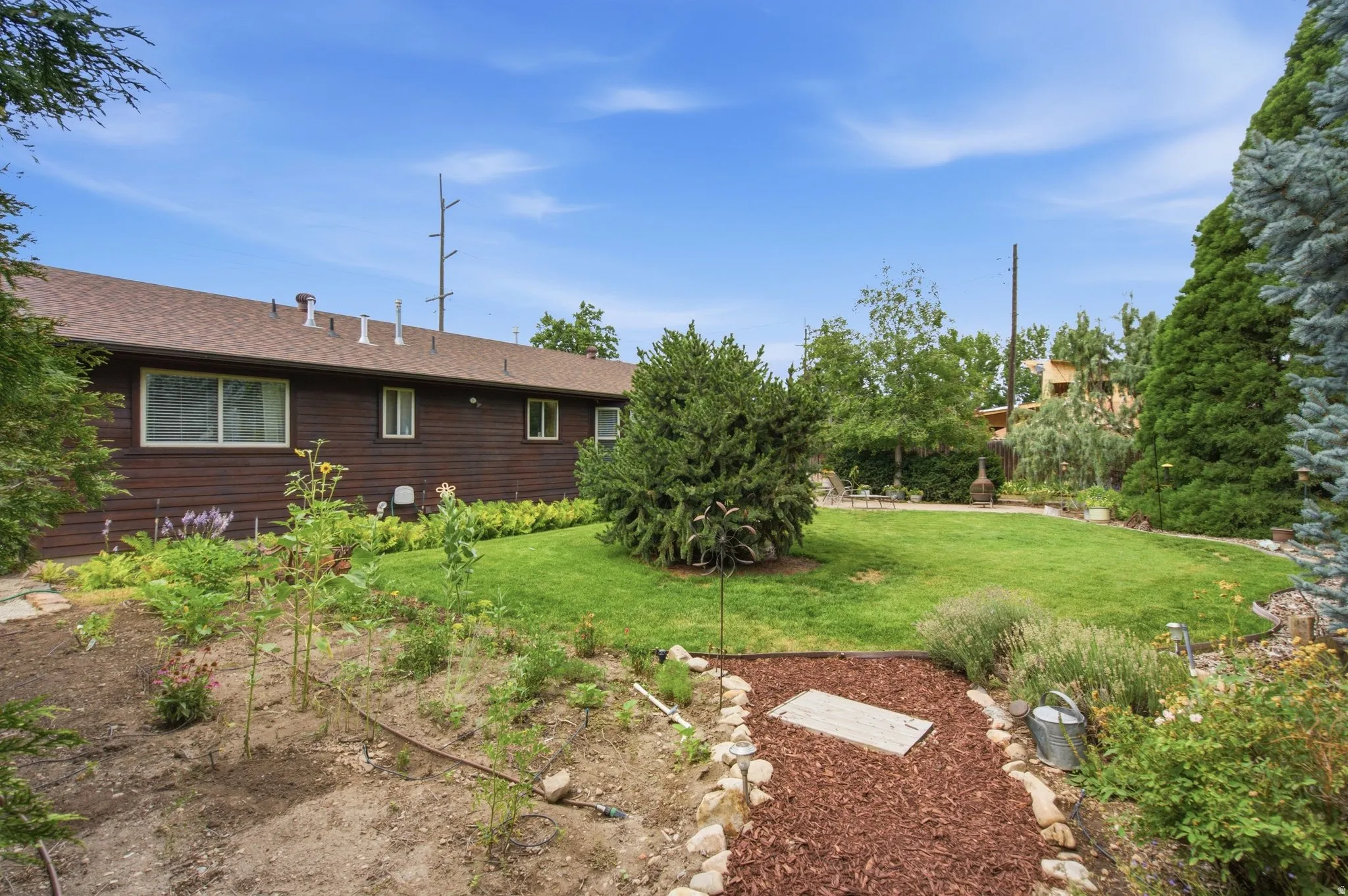 Expansive backyard featuring a manicured lawn, established garden beds, natural stone accents, and mature trees
