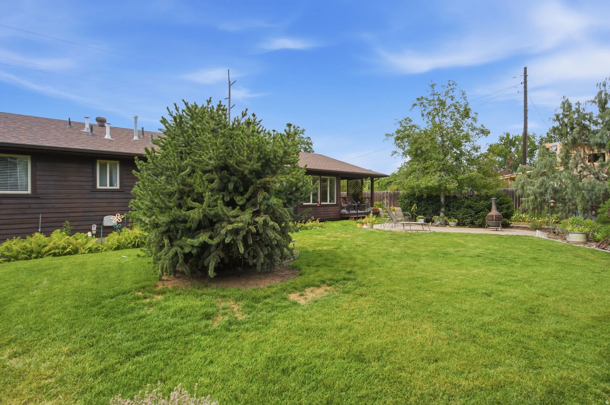 Expansive green lawn with mature landscaping, featuring a paver patio and covered porch