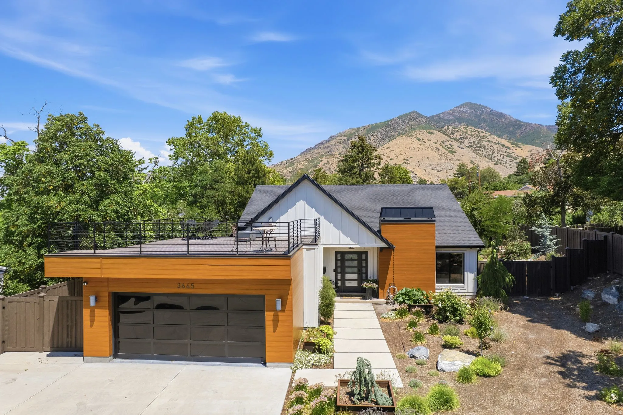 Contemporary house exterior featuring a wood-painted metal panel accent wall, board and batten siding, and a glass-door garage with a deck over it.
