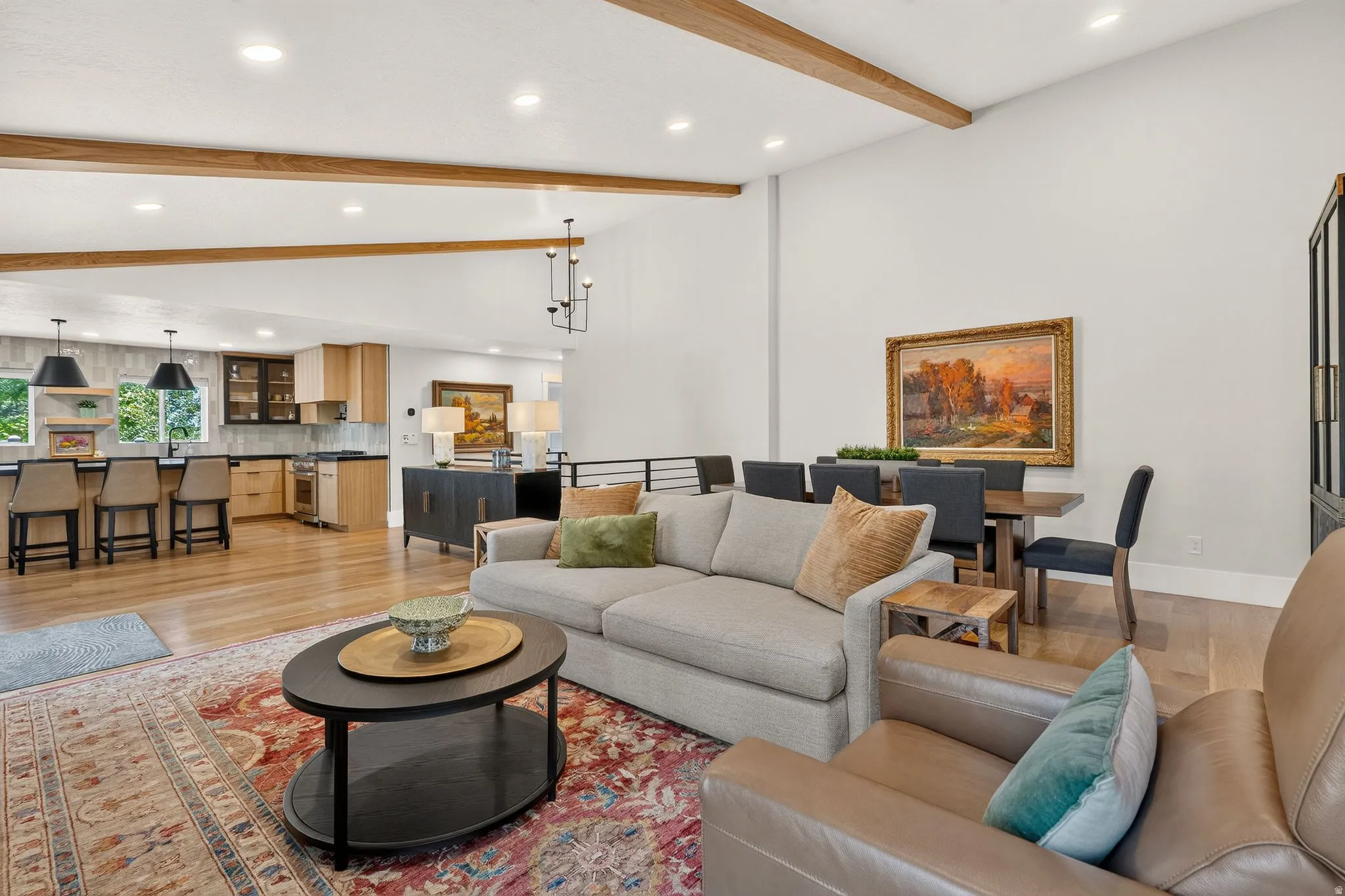 Open-concept living area featuring wood-finish flooring, exposed ceiling beams, recessed lighting, and a kitchen with an island and pendant lighting