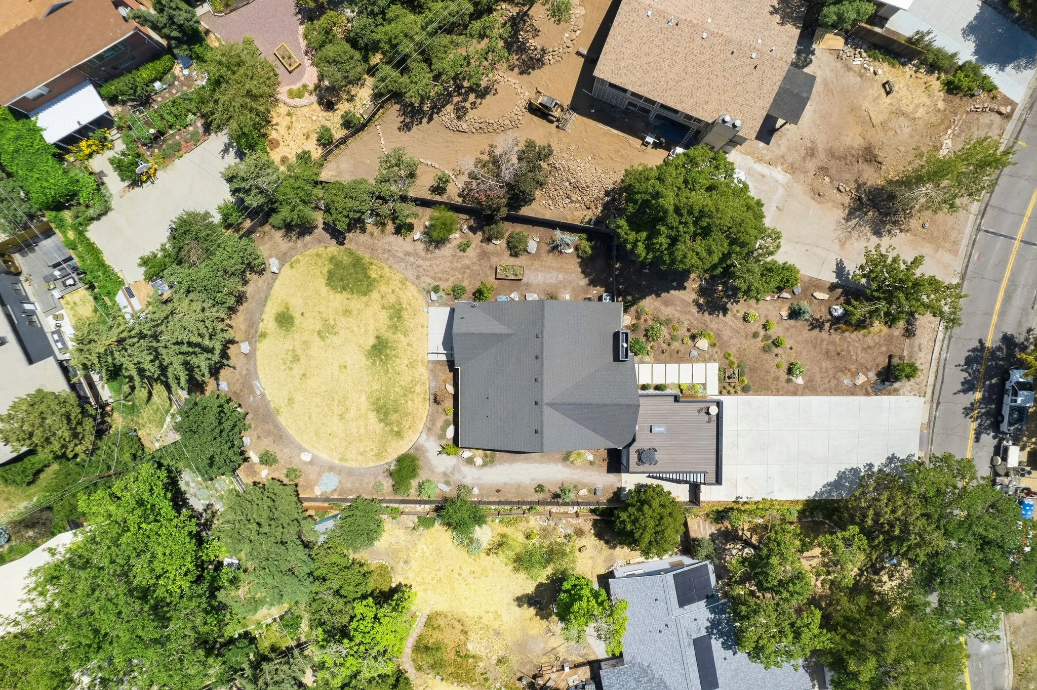 Contemporary residence featuring a dark gray roof, an expansive concrete driveway, backyard, and a large wooden deck over a garage.