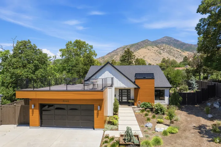 Contemporary house exterior featuring a wood-painted metal panel accent wall, board and batten siding, and a glass-door garage with a deck over it.