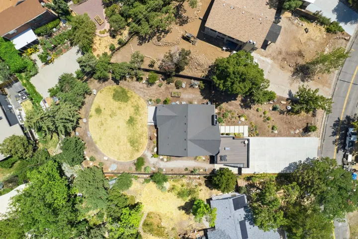 Contemporary residence featuring a dark gray roof, an expansive concrete driveway, backyard, and a large wooden deck over a garage.