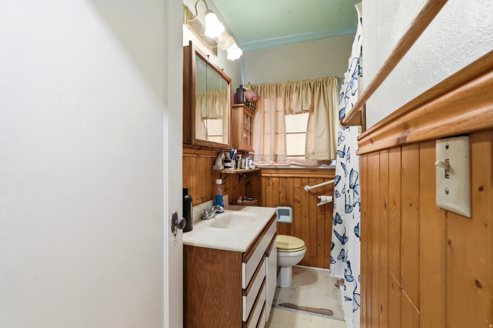Bathroom featuring wood paneling, a single vanity with a solid surface countertop, an overhead mirrored medicine cabinet, and a window with natural light