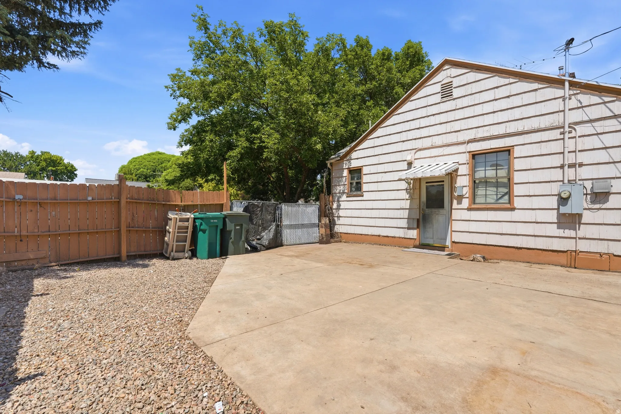Exterior side of the property featuring white horizontal siding, a concrete patio, and a gravel-covered area