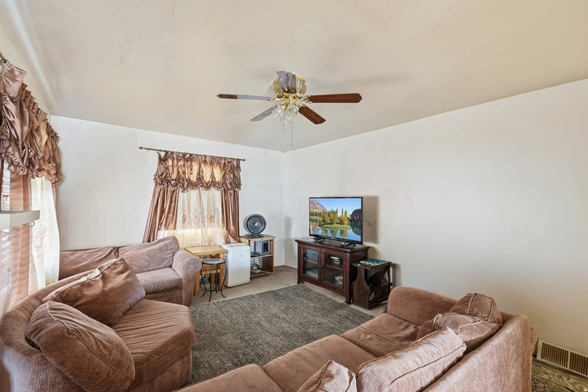 Living area featuring a ceiling fan with integrated lighting, multiple windows with blinds and valances, and light-toned walls