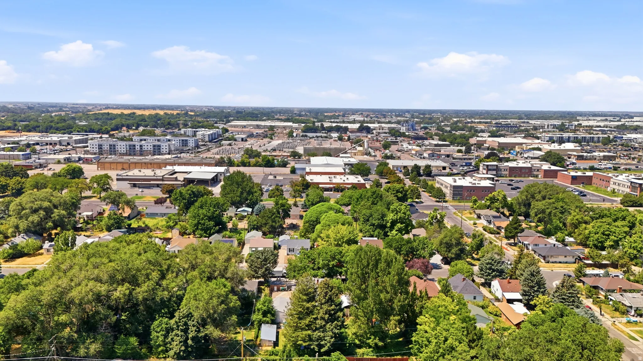 Expansive aerial perspective showcasing a residential area with mature tree coverage and established homes, bordered by commercial and mixed-use buildings