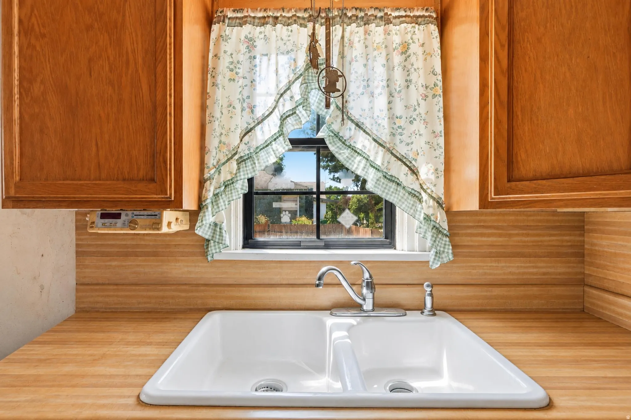 Kitchen sink area featuring a double basin sink, chrome faucet, wood-finish countertops, natural wood cabinetry, and a window with exterior views