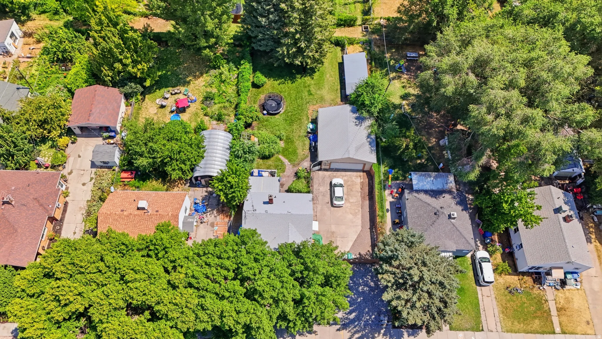 Aerial perspective showcasing a residential property with a detached garage, a long driveway, a greenhouse structure, and substantial green space with mature trees