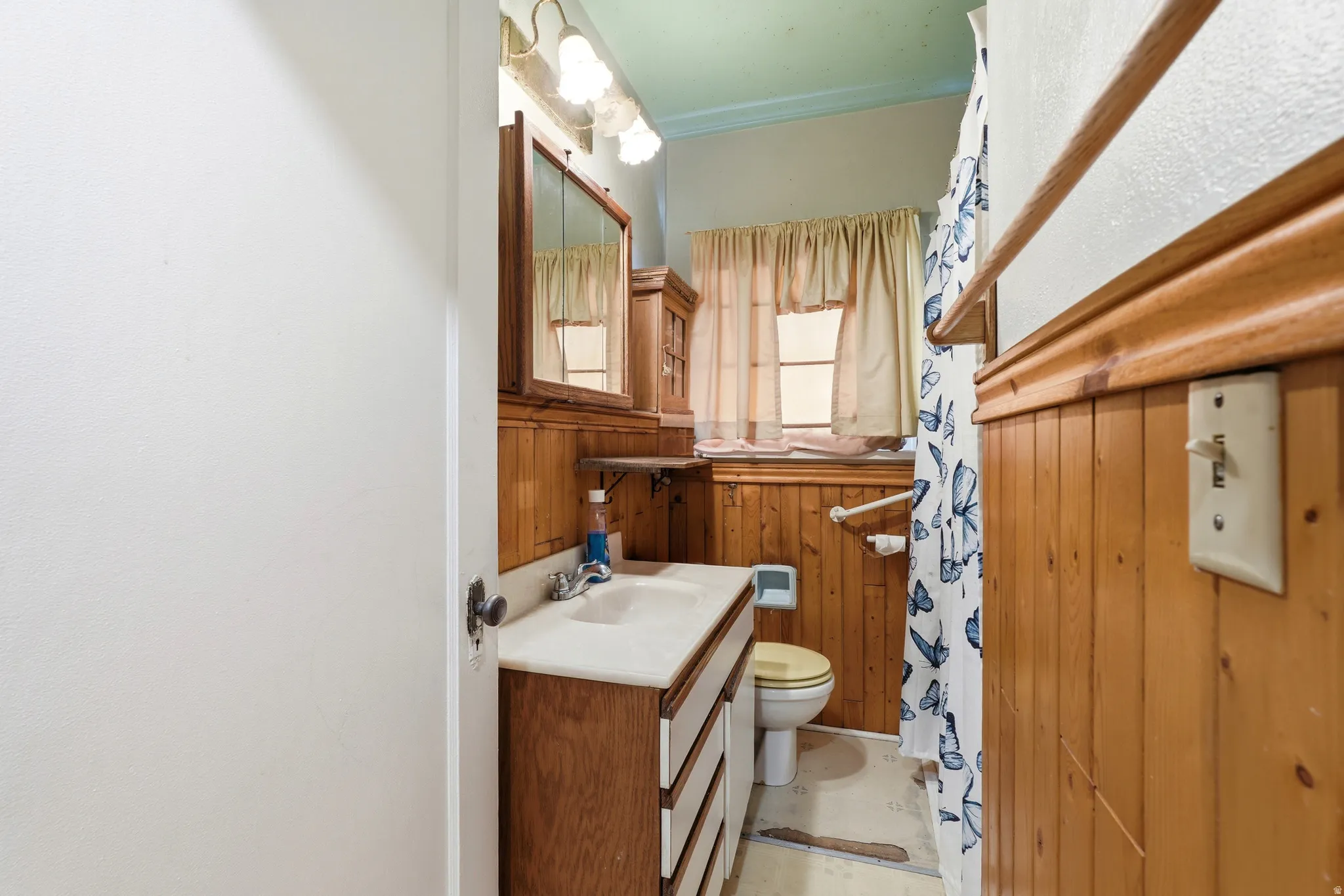Bathroom featuring wood paneling, a single-sink vanity with a light-colored countertop, and a medicine cabinet with mirrored doors