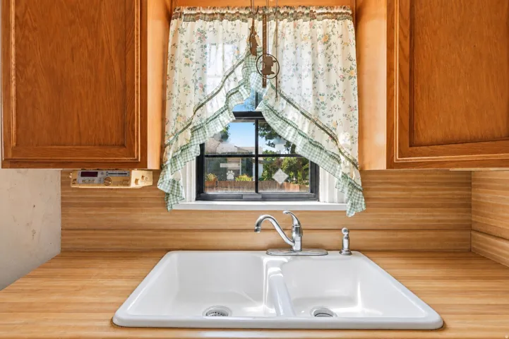Kitchen sink area featuring a double basin sink, chrome faucet, wood-finish countertops, natural wood cabinetry, and a window with exterior views