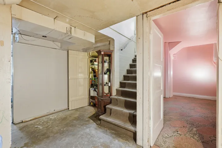 Basement area featuring a carpeted staircase with white risers, a sealed concrete floor, and a separate room with pink walls and patterned carpeting