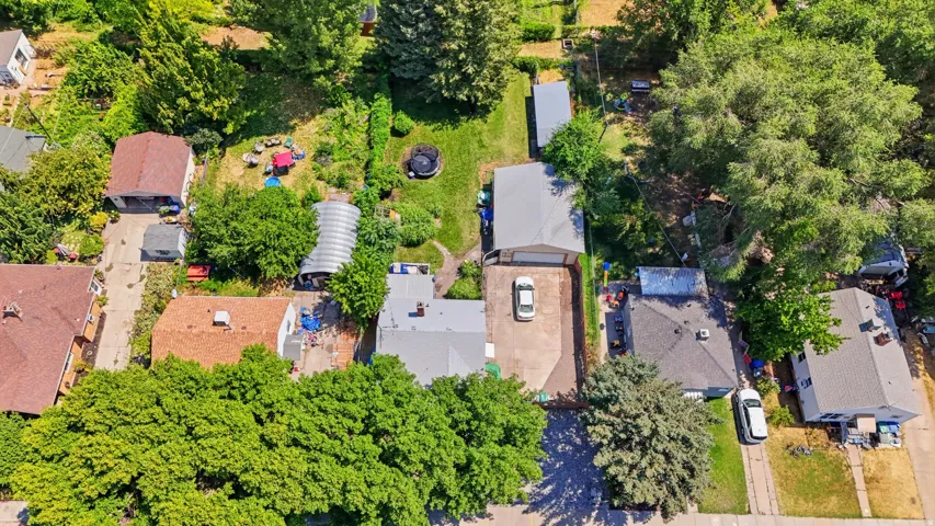 Aerial perspective showcasing a residential property with a detached garage, a long driveway, a greenhouse structure, and substantial green space with mature trees