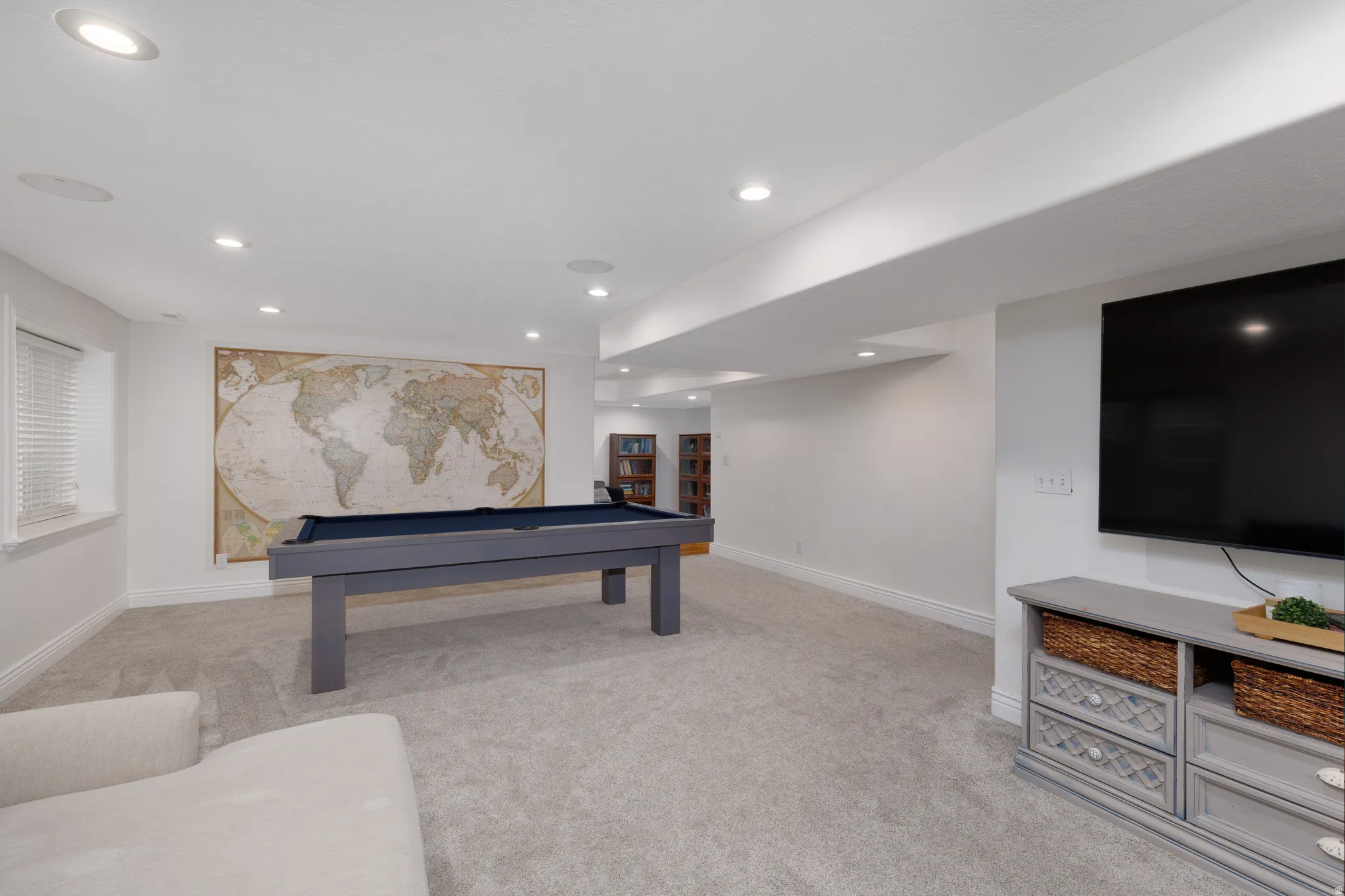 Spacious recreation room featuring recessed lighting, light gray carpeting, and a window with blinds