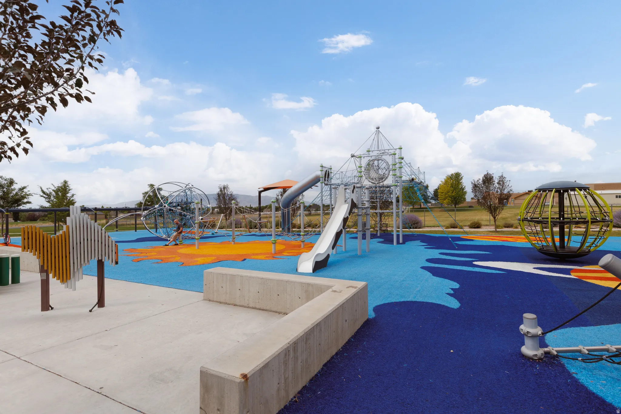 Expansive playground featuring a soft-surface ground, multiple slides, climbing structures, and concrete seating
