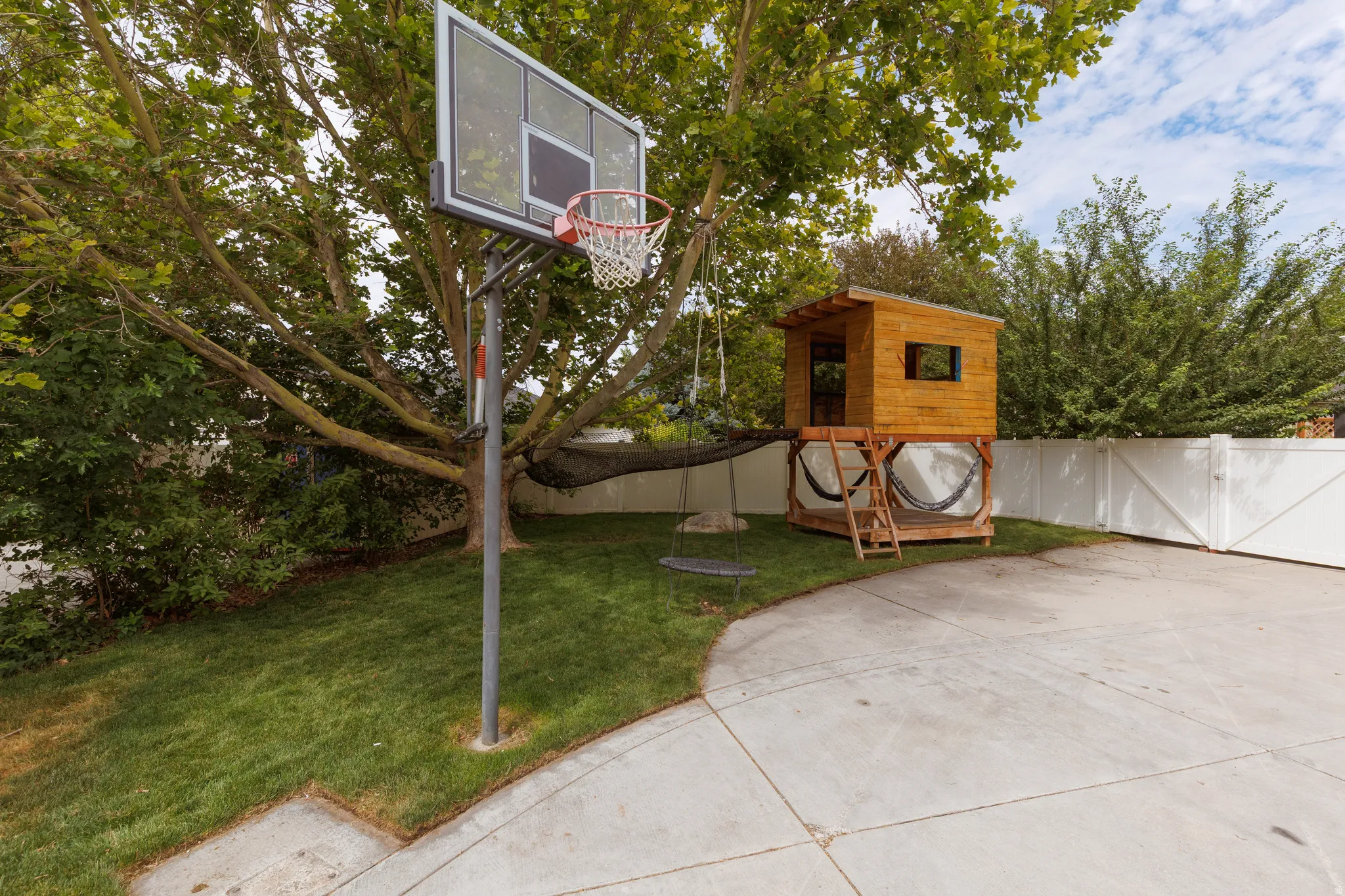Expansive backyard featuring a basketball hoop, manicured lawn, and mature trees