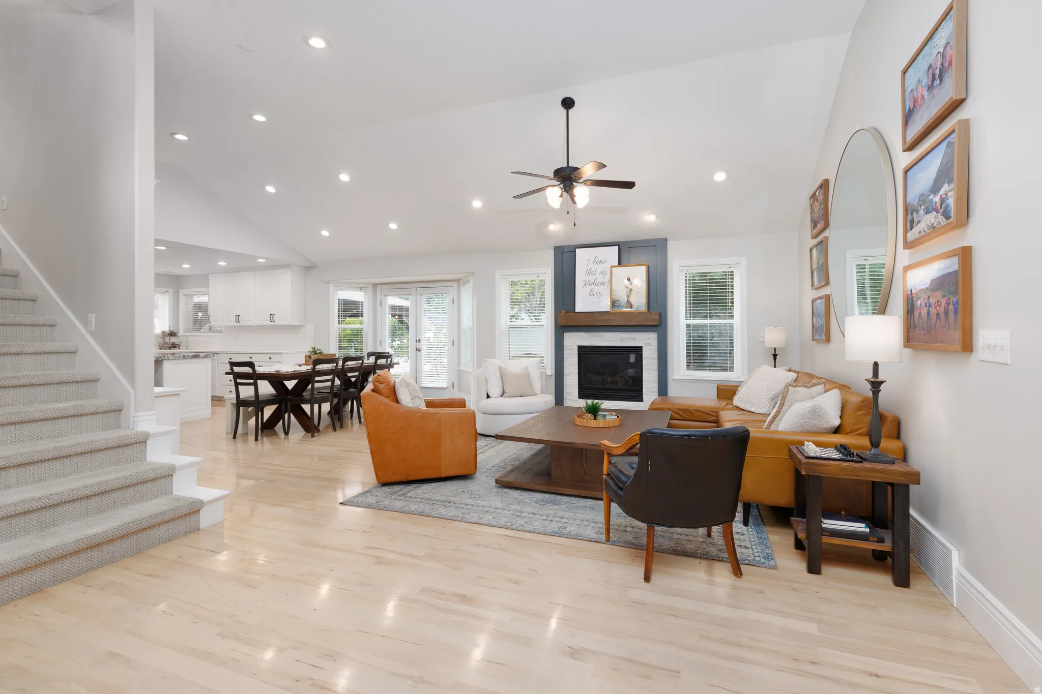 Open-concept living area featuring light wood-finish flooring, a vaulted ceiling with recessed lighting, and a dark wood ceiling fan