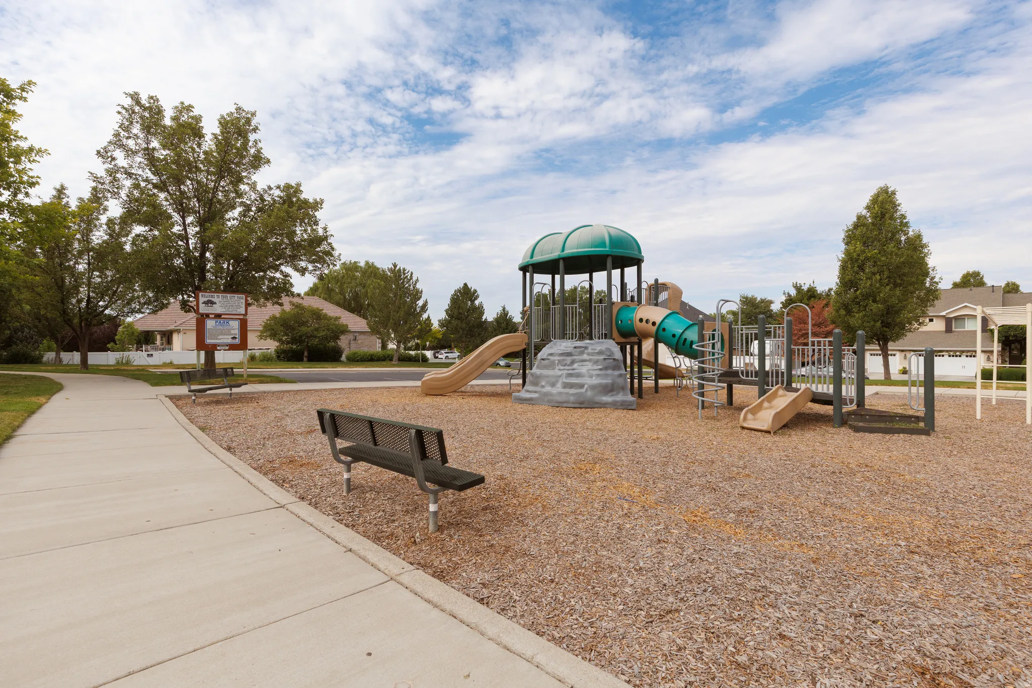 Community playground featuring a multi-level play structure with slides and climbing elements, surrounded by woodchip surfacing